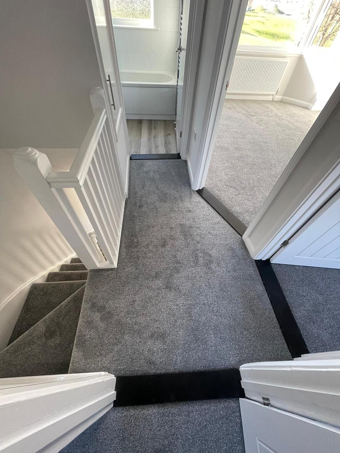 Grey carpet fitted across a landing and down the stairs, finished at each doorway with a threshold bar
