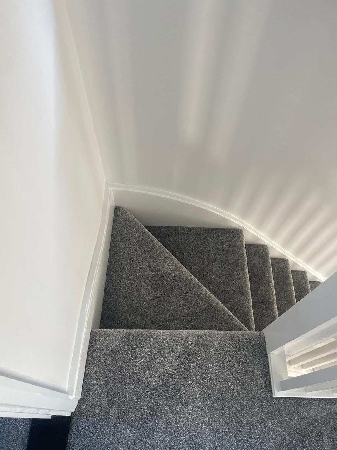 Grey carpet fitted to winder stairs, each tapered tread cut and folded to the turn