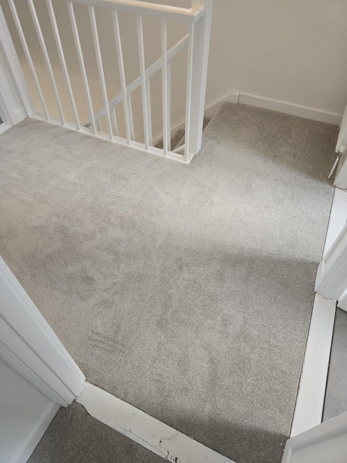 Pale carpet fitted across a landing, cut round the balustrade and into the doorways
