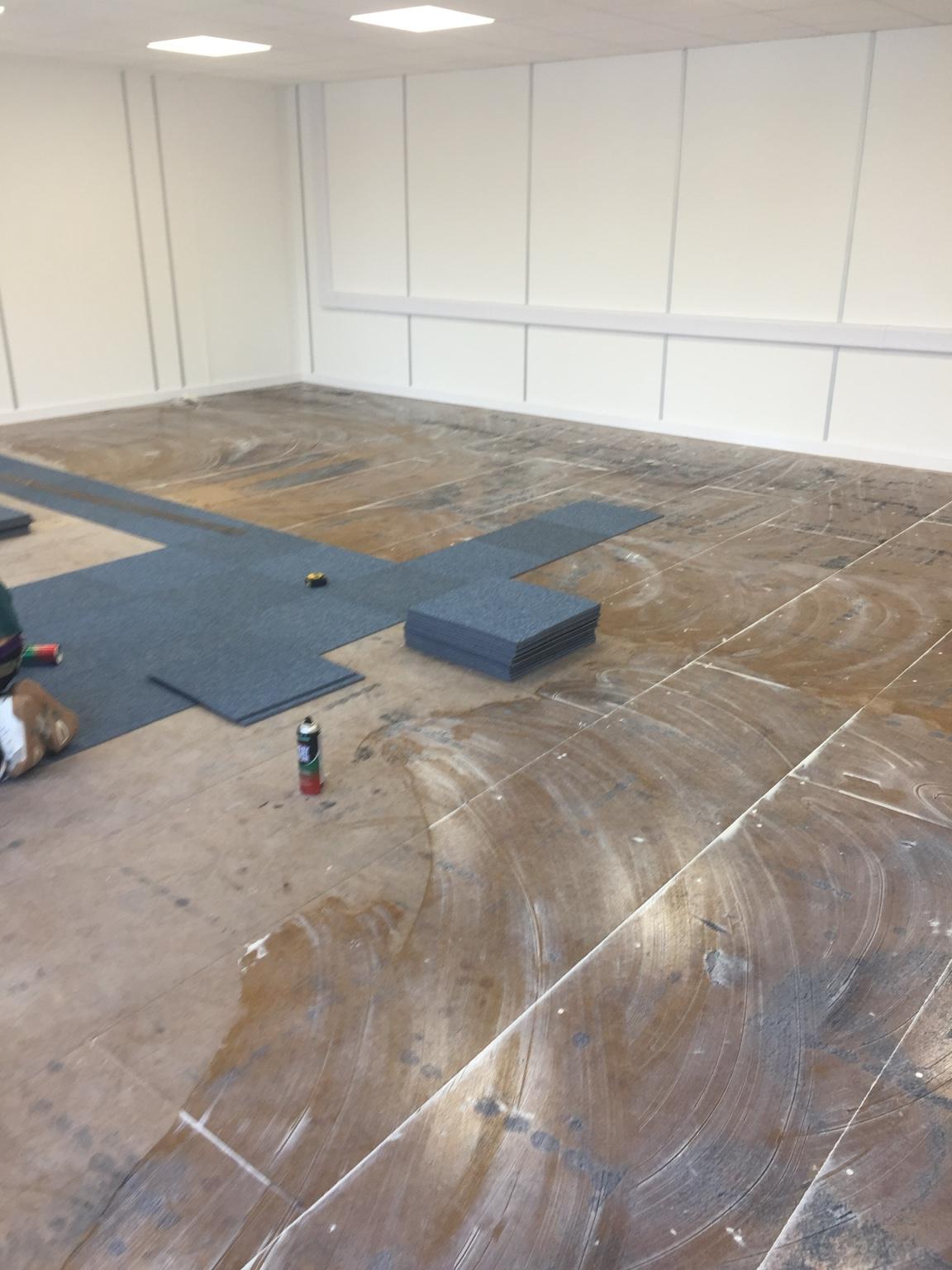 During installation: a subfloor marked out with snapped lines, a run of carpet tiles laid out across it and a stack waiting alongside