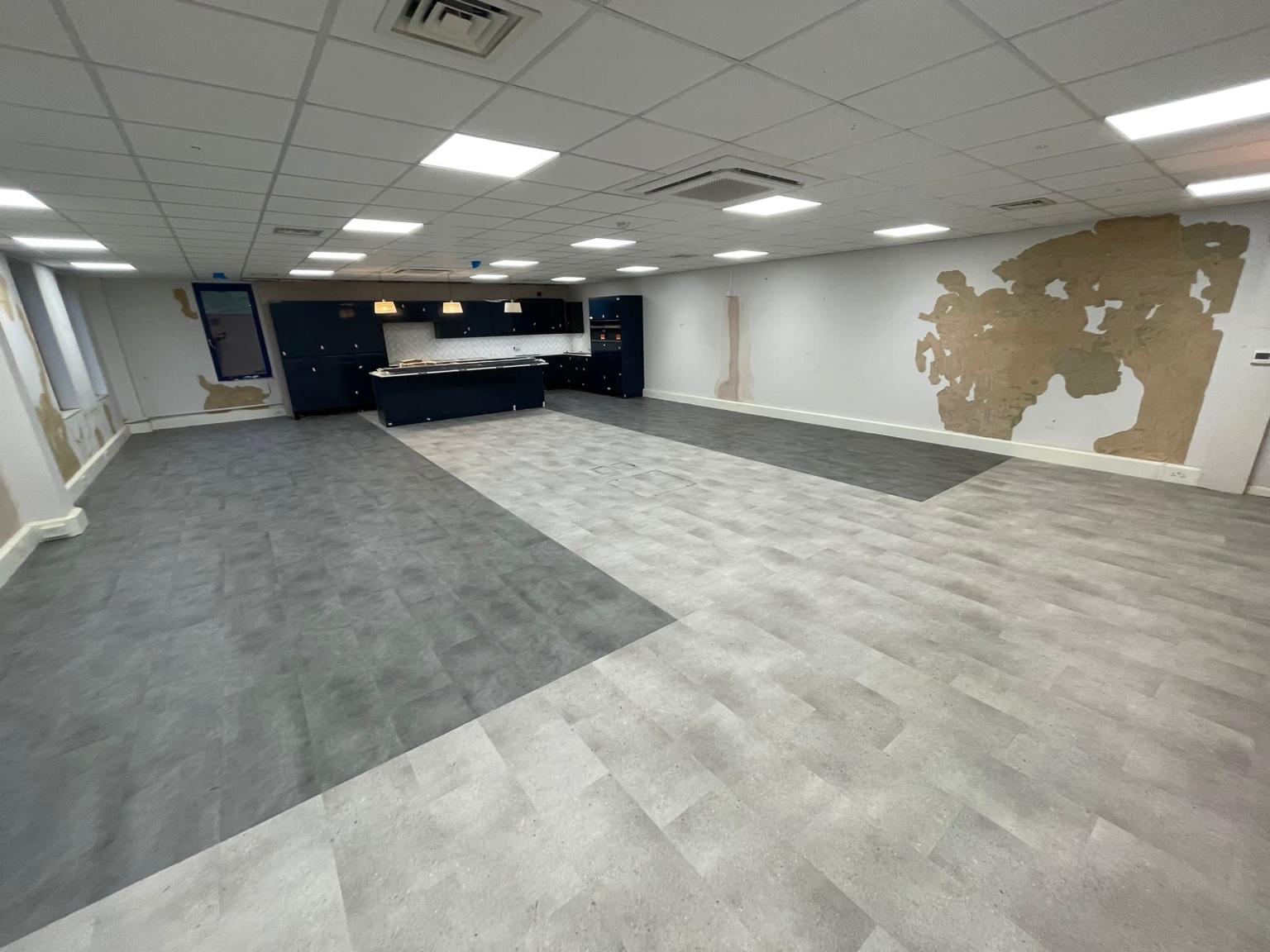 The full width of the finished commercial vinyl floor, the darker and lighter areas turning through the room under a suspended ceiling