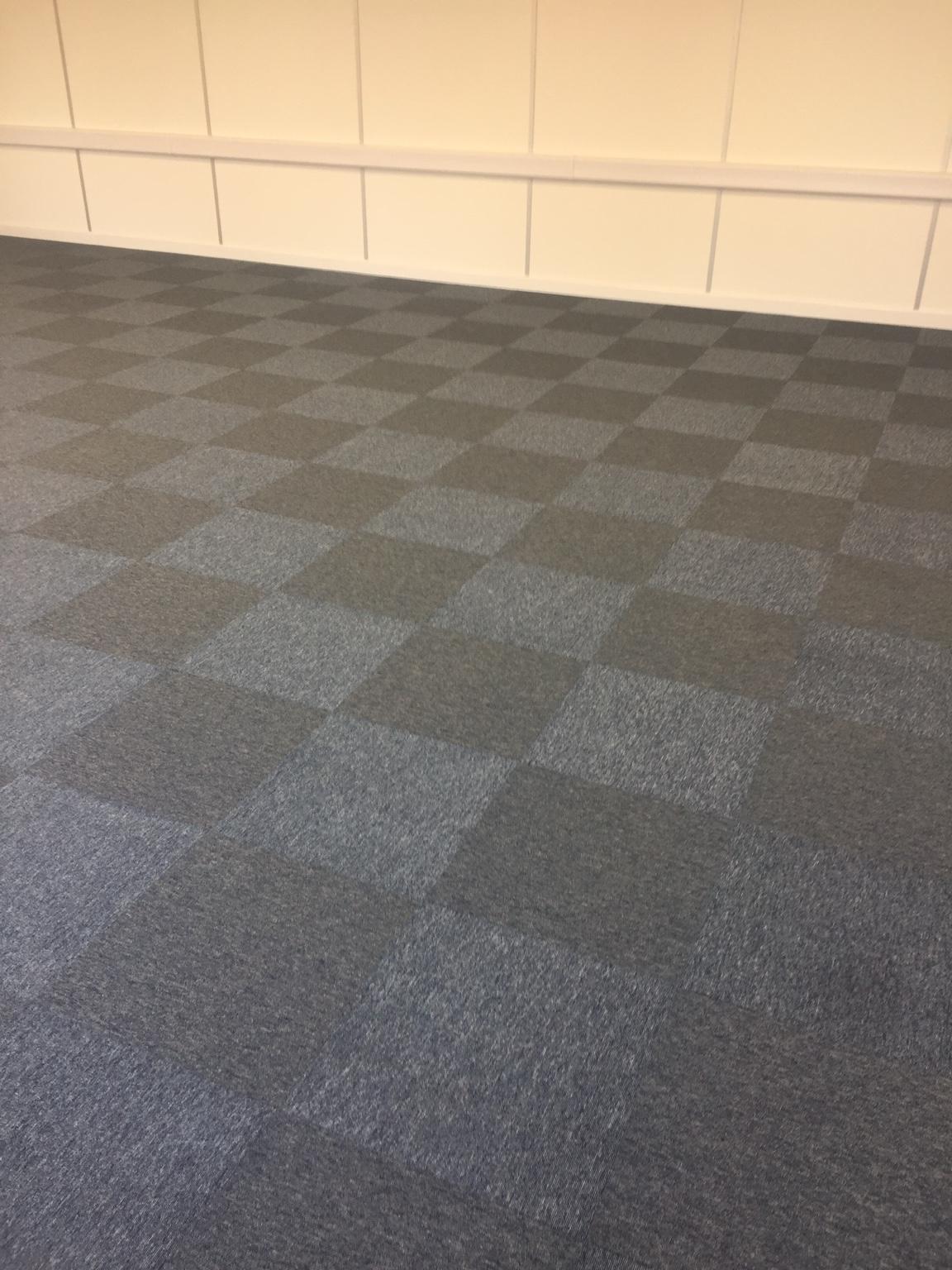Close view of the finished carpet tiles, alternate squares catching the light differently so the floor reads as a chequerboard