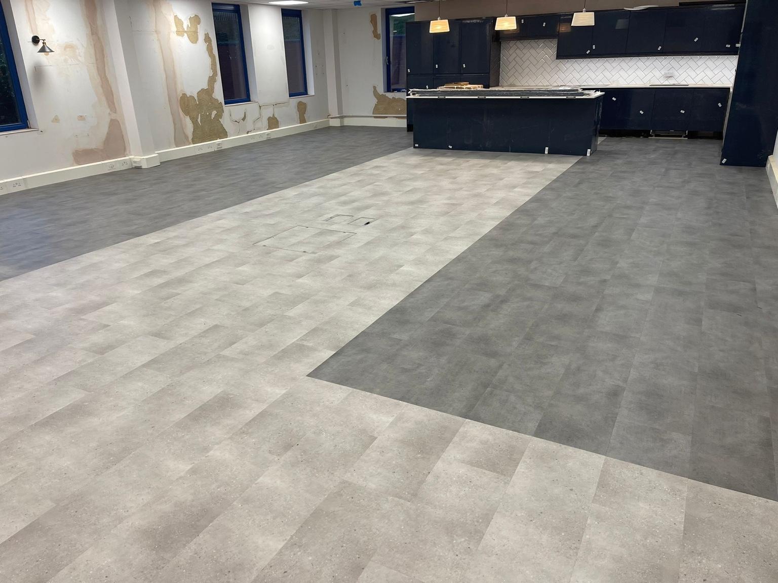 The finished commercial vinyl floor across an open room, a darker grey field meeting a lighter speckled one along a straight line, with a fitted counter and cabinets beyond